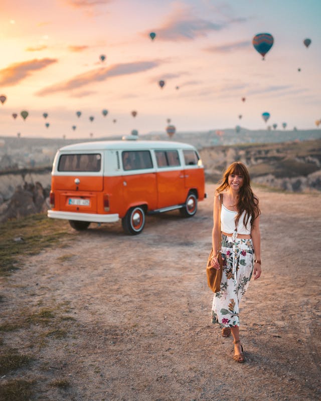 Smiling woman in a floral skirt and white crop top, embracing boho-chic enjoying in holidays outfit against a dreamy sunset backdrop.