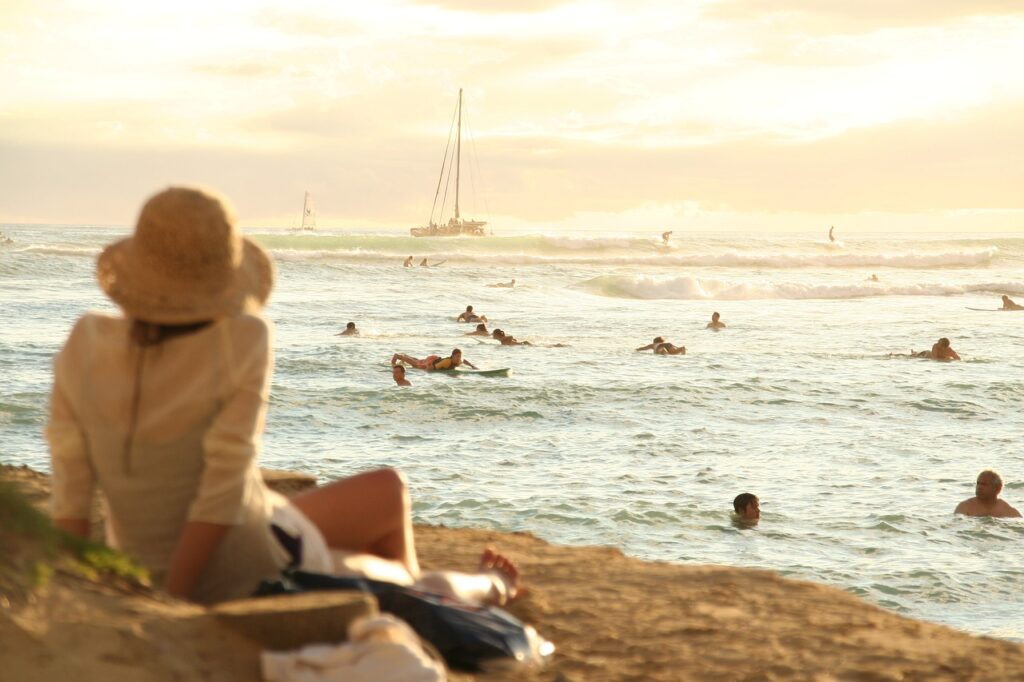 Women wearing hat sitting on a beach enjoying her vacation.